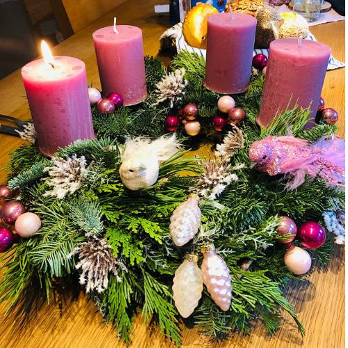 Weihnachten ohne Stress. Das Bild zeigt einen Adventskranz mit der ersten brennenden Kerze. Innehalten und in das Kerzenlicht schauen kann ein gutes Ritual sein, um achtsam und bewusst in den Tag zu starten.