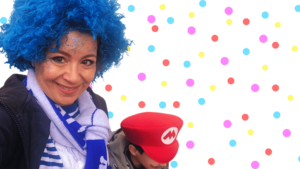 Freude entdecken im Karneval. Das Foto zeigt Pia Hübinger, die Verfasserin des Artikels, mit einer blauen Perücke und einem blau-weißen Ringelshirt mit ihrem Sohn, von dem man jedoch nur die Supermario-Kappe sieht.