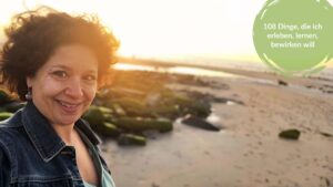 Pia Hübinger am Strand im warmen Abendlicht, lächelnd mit dem Wind im Haar; im Bild der Titel: 108 Dinge, die ich erleben, lernen und bewirken will.
