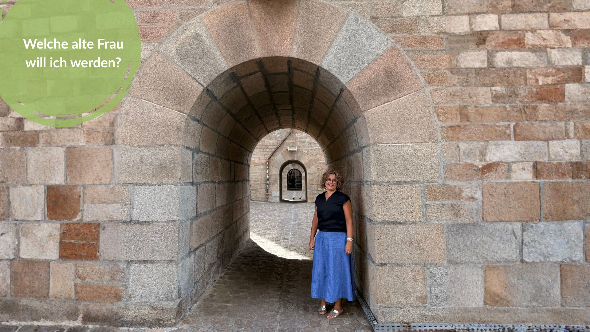 Das Bild zeigt Pia Hübinger in einem Bogengang stehen. Es trägt den Titel: Great Ager: Welche alte Frau will ich werden?